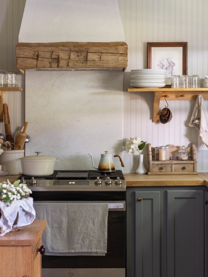 Range under a plaster hood with wood beam, beadboard walls, peg rail, blue cabinets