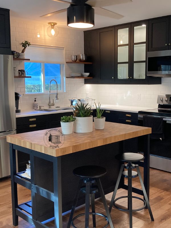 Black IKEA cabinets, white subway tile and a butcher block island with two stools