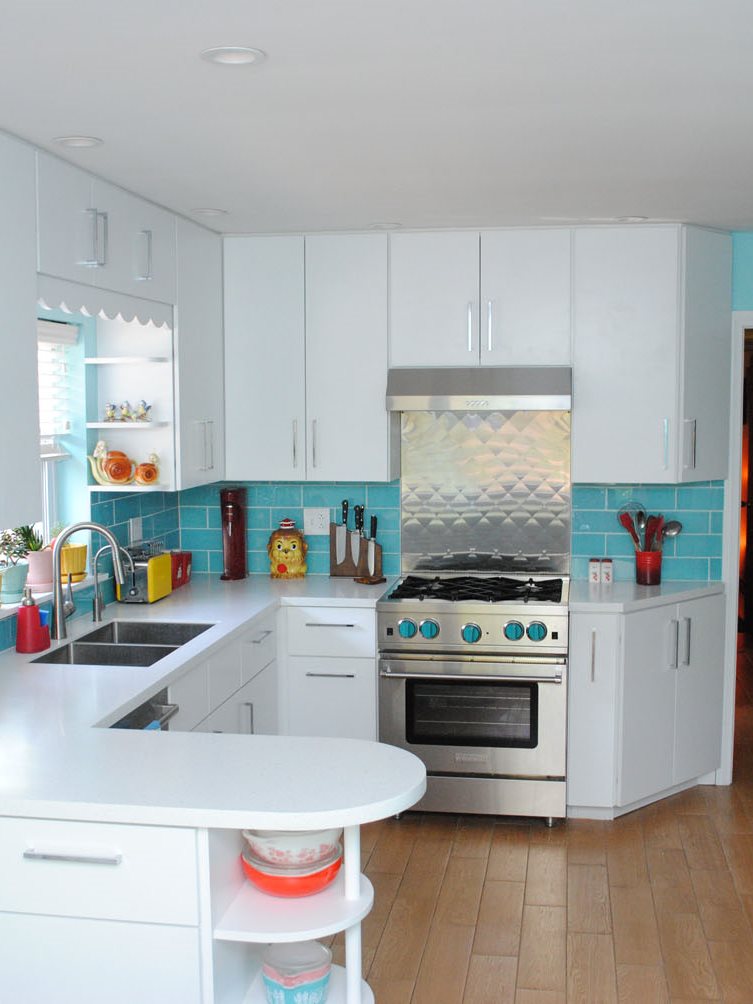 White flat-front cabinets, aqua glass tile, stainless range backsplash, rounded peninsula with shelves