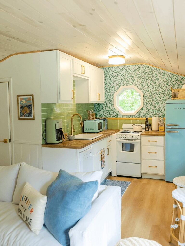 Tiny cottage kitchen with green tile, botanical wallpaper, octagon window and blue retro fridge
