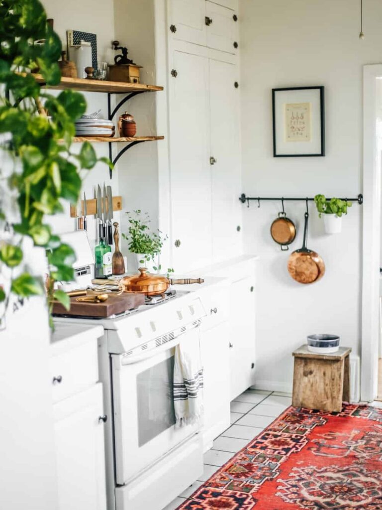 Narrow white galley with wood shelves, copper pans on black rail, red rug